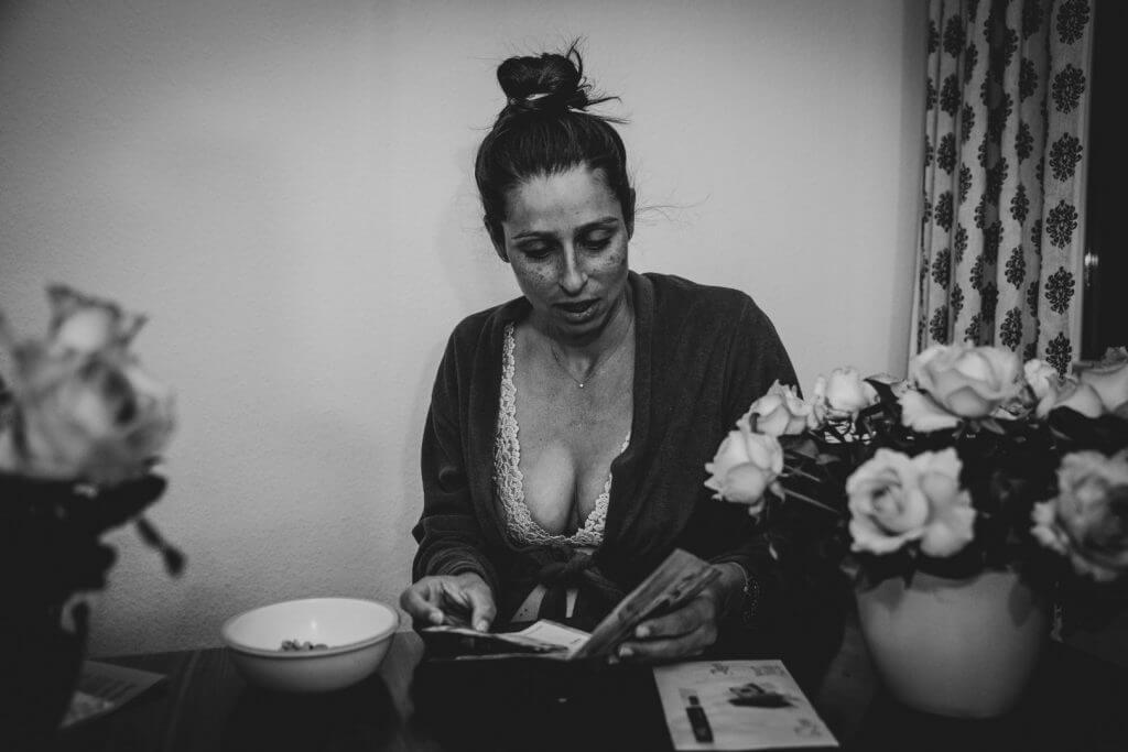 Frau im Bademantel sitzt zwischen Rosen und liest Karte