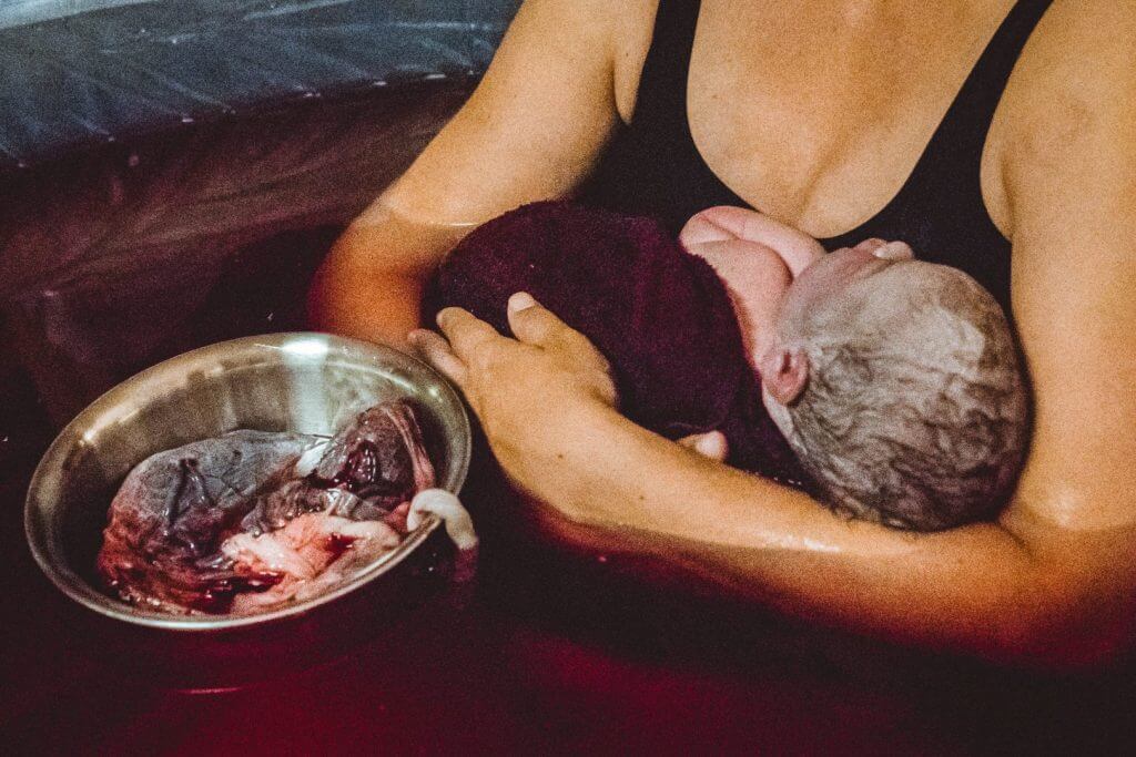 Neugeborenes im mütterlichen Arm mit Plazenta in Schüssel