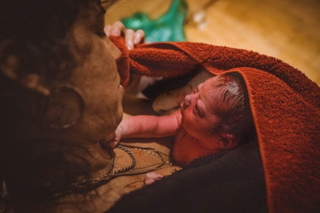 Neugeborenes Baby schaut Mutter aus rotem Handtuch an.
