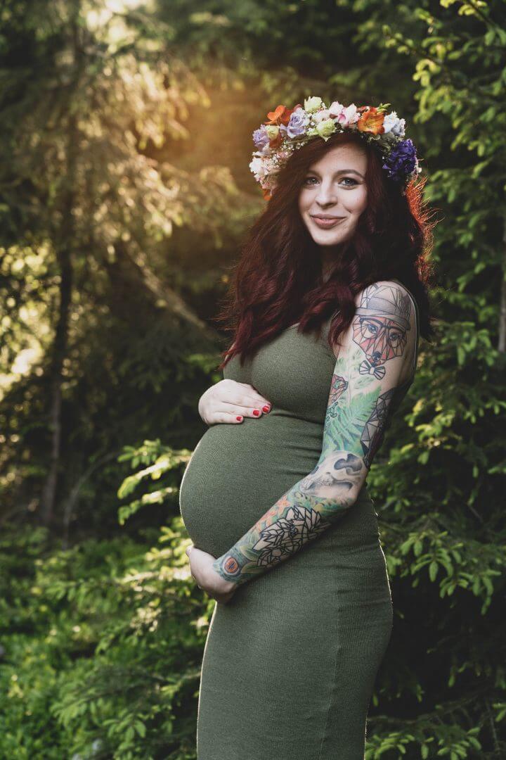 Schwangere steht mit Blumenkranz im Wald