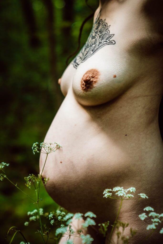 Nackter Babybauch mit Tattoos im Wald
