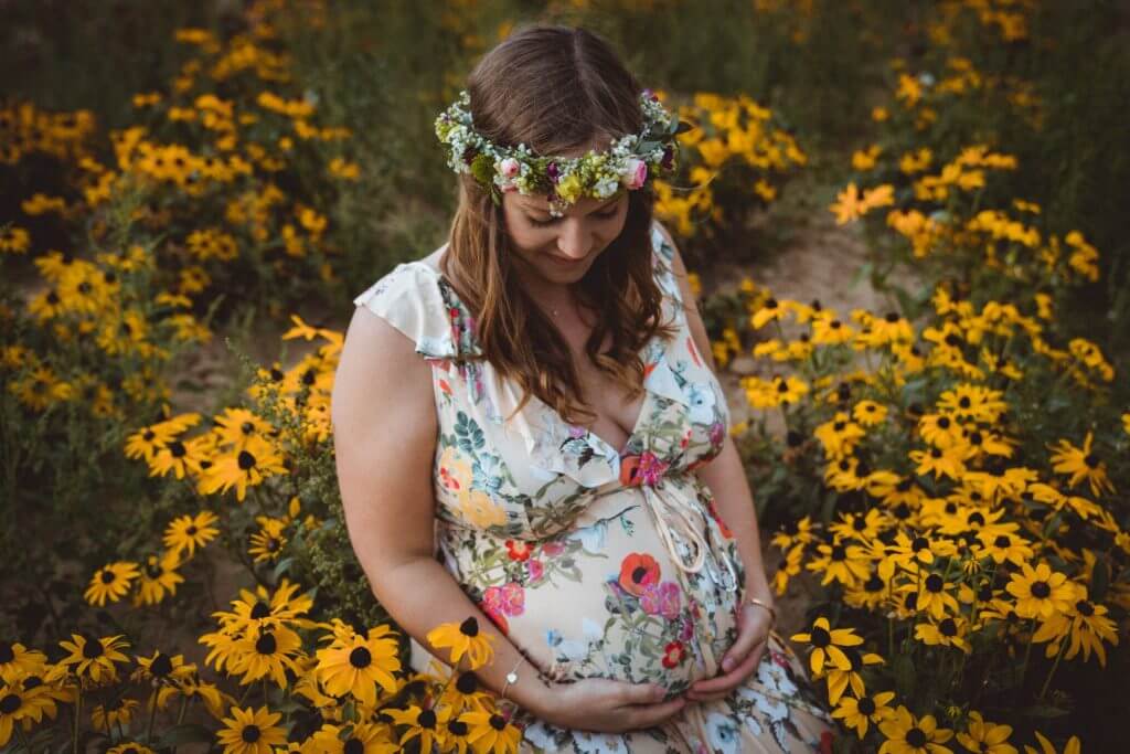 Schwangere kniet in gelbem Blumenfeld