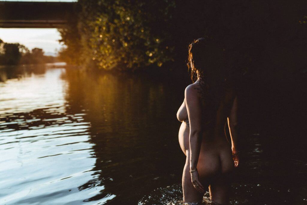 Schwangere läuft Richtung Sonnenuntergang im Wasser