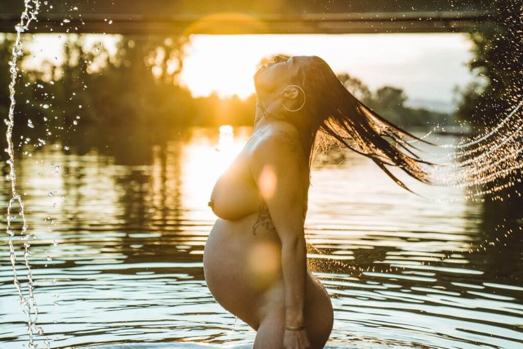 Schwangere schwingt ihr nasses Haar im Sonnenuntergang