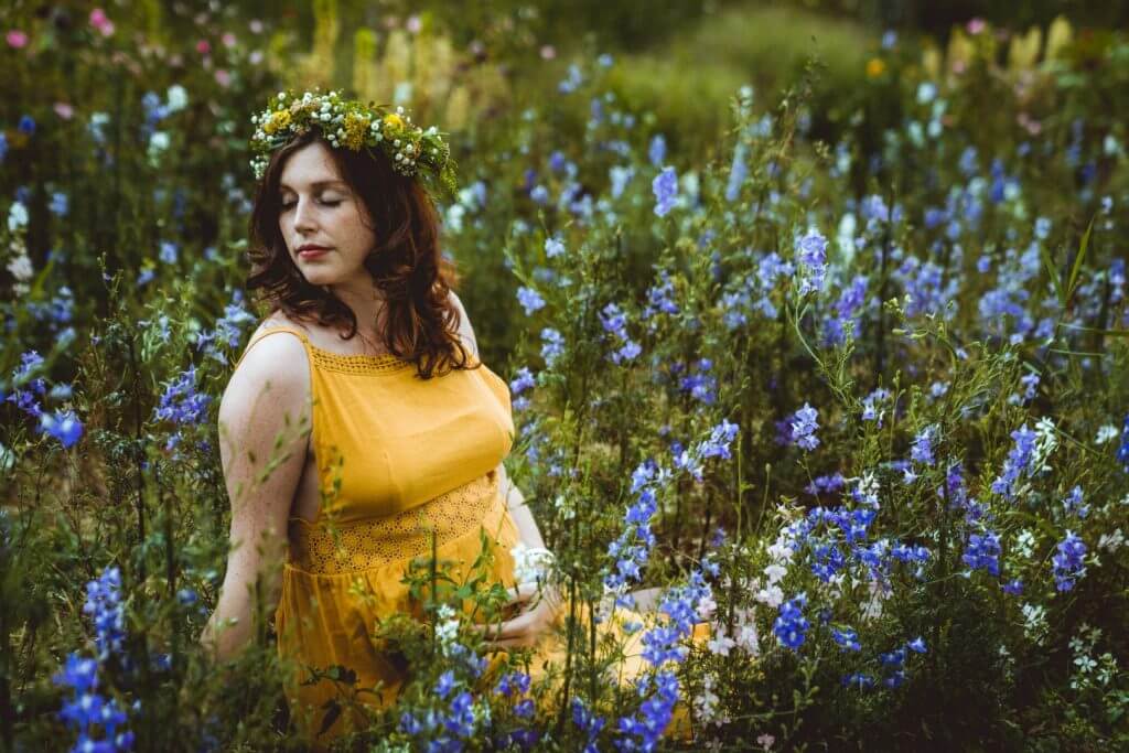 Schwangere sitzt in blauem Blumenfeld