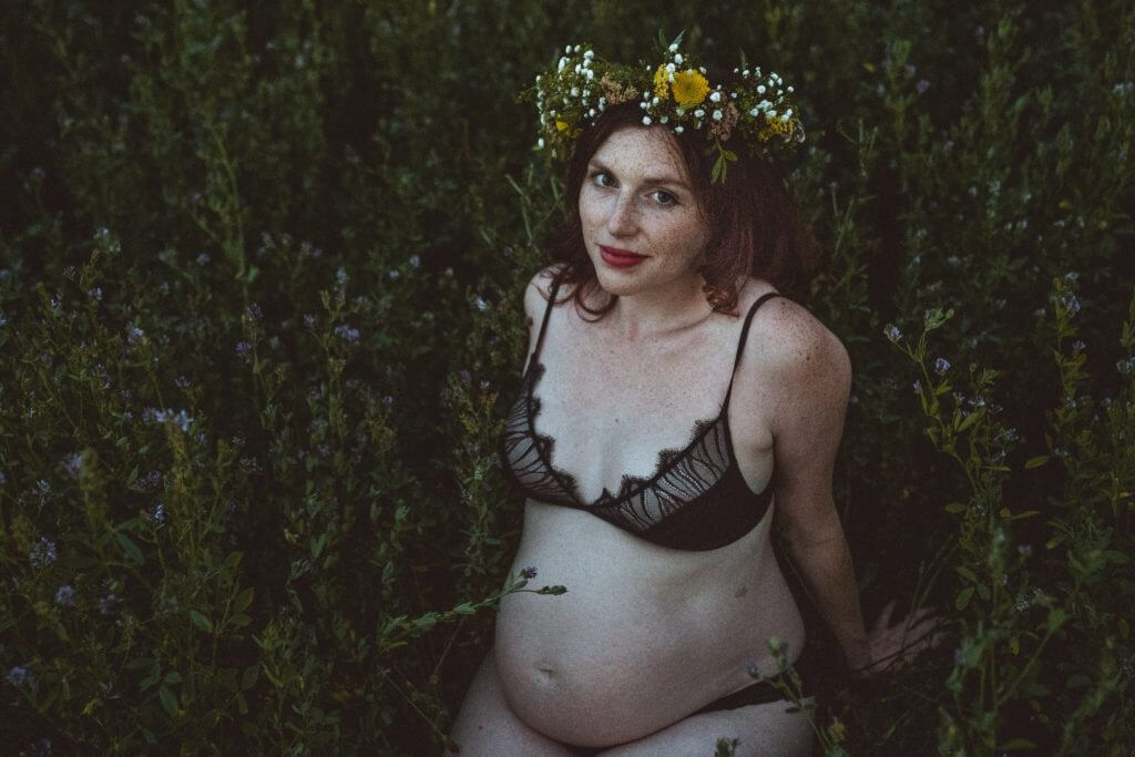 Schwangere sitzt in Unterwäsche auf Wiese