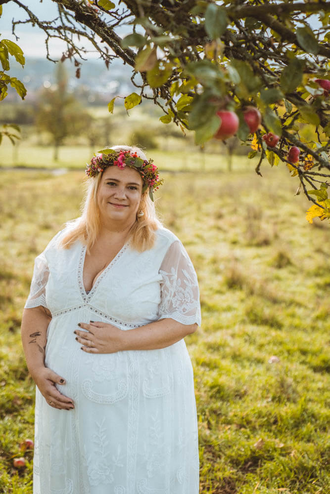 Schwangere streicht Babybauch unter Apfelbaum