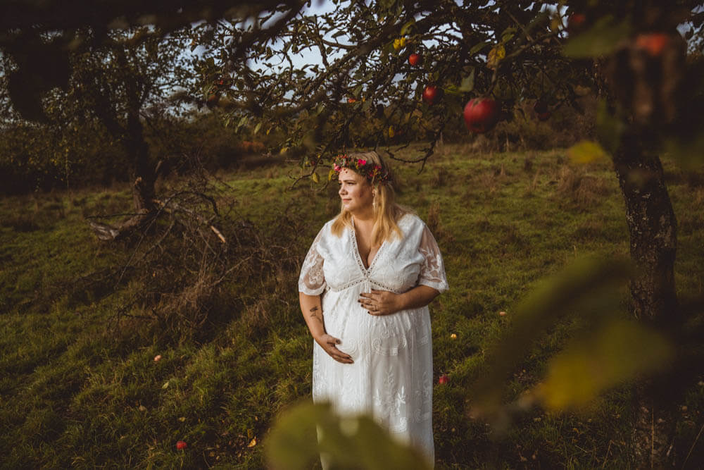 Schwangere streichelt Babybauch unter Apfelbaum