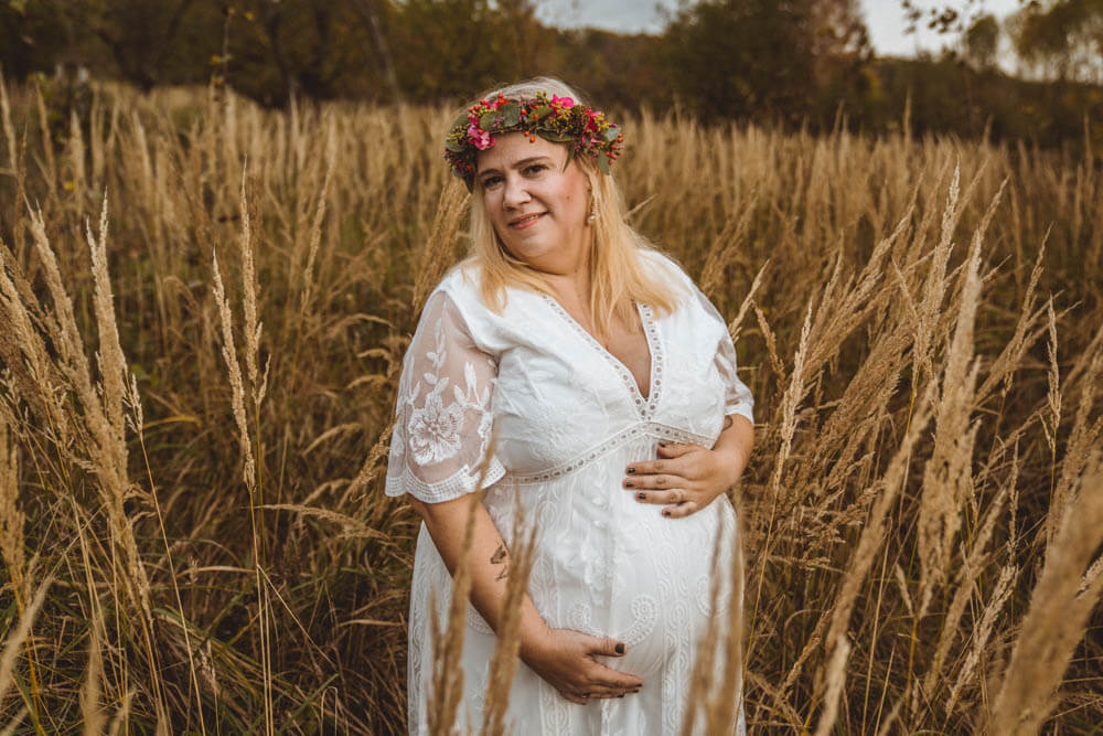 Schwangere in weißem Kleid mit Blumenkranz steht in Getreideähren