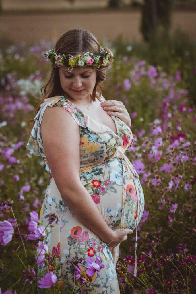 Schwangere steht in Blumenfeld und streichelt Babybauch