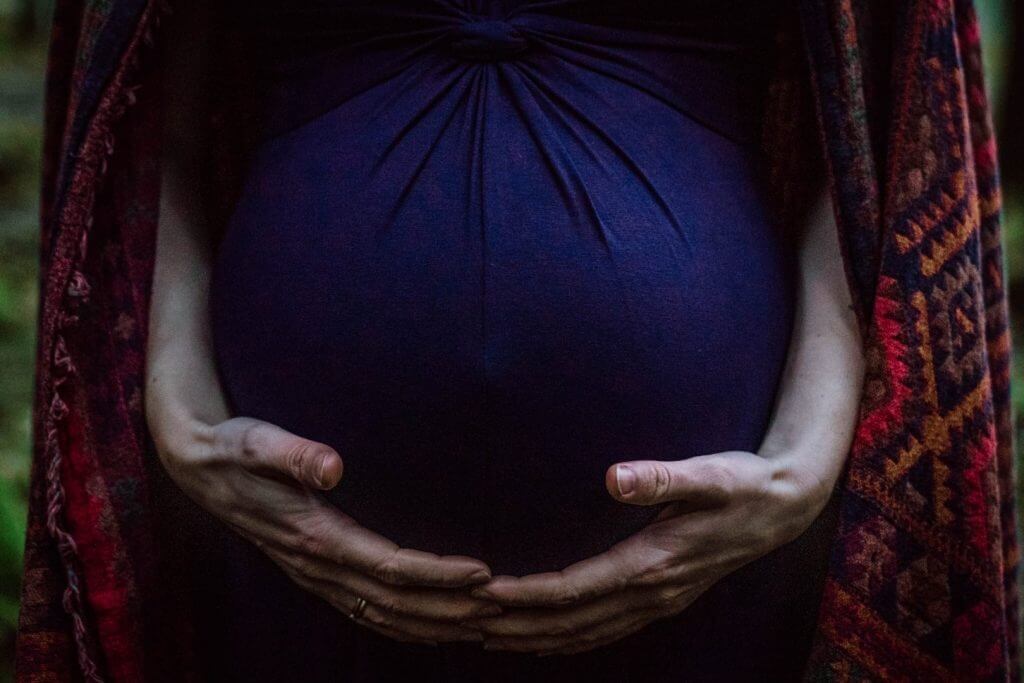 Babybauch in blauem Kleid wird gehalten.