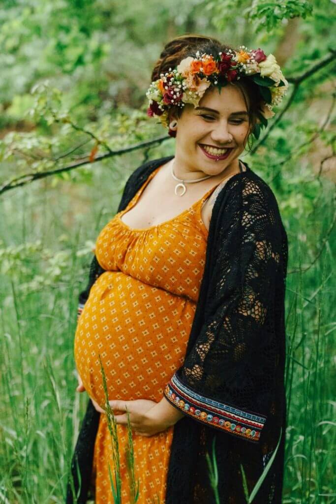 Schwangere steht im Wald und hält lachend Bauch