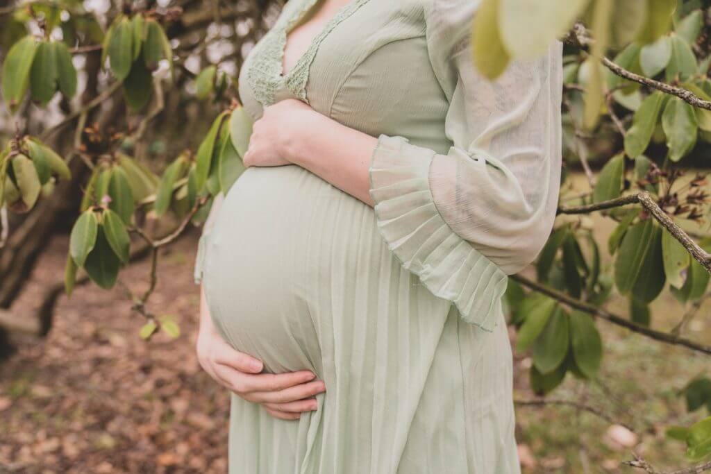 Nahaufnahme Babybauch in lindgrünem Kleid vor Büschen