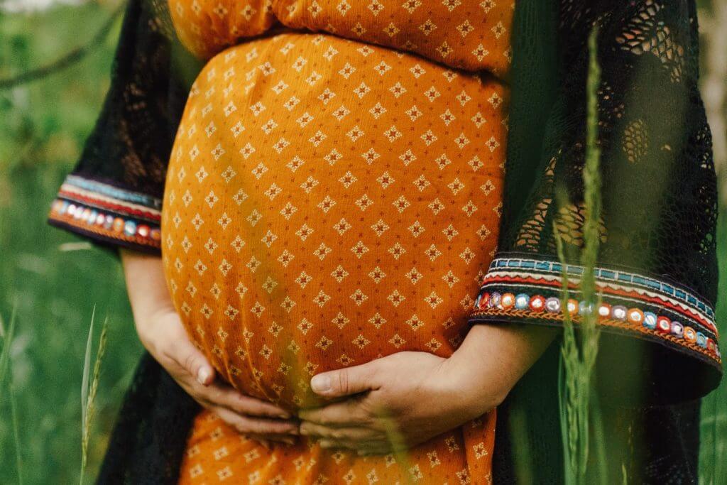 Nahaufnahme Babybauch in orangenem Kleid in Gräsern
