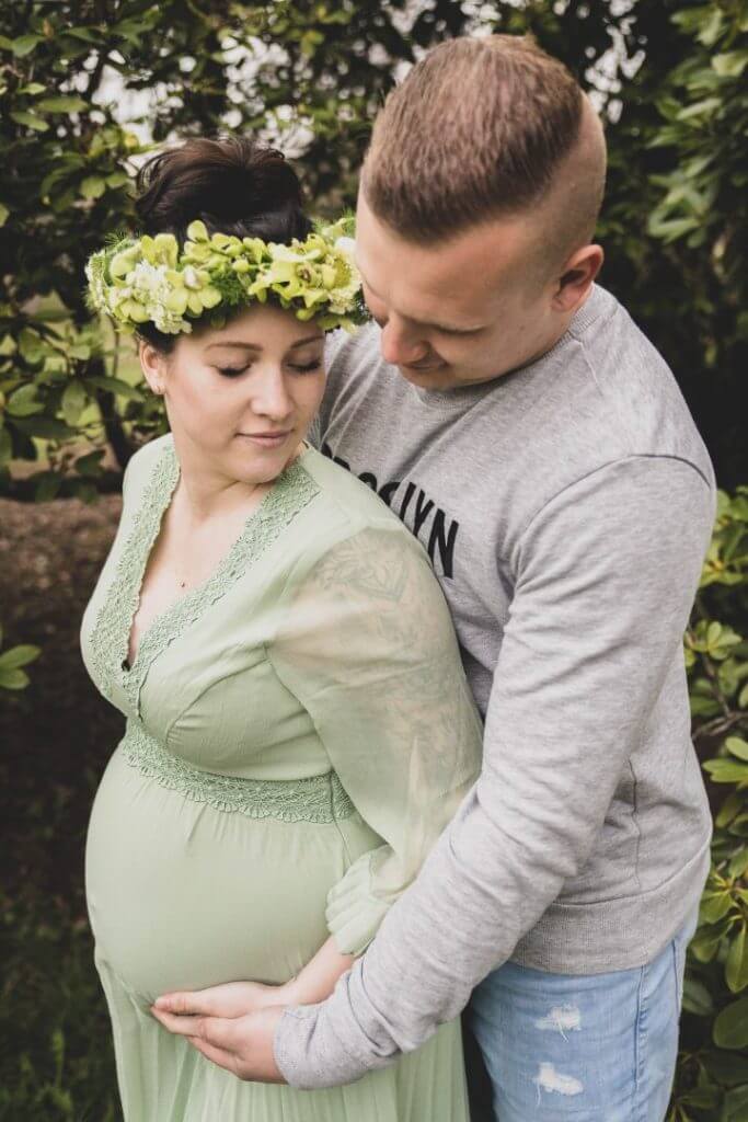 Werdender Vater hält Schwangere vor Bäumen im Arm