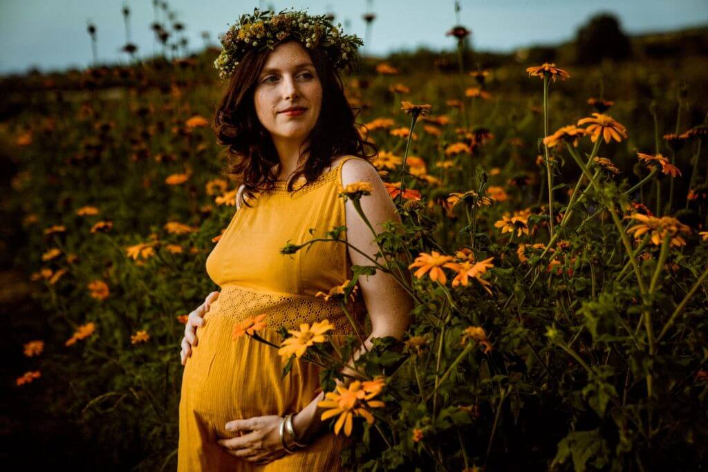 Schwangere steht vor orangenen Blumen und hält Babybauch