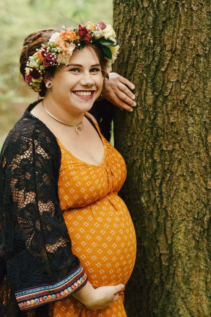 Schwangere lehnt an Baum und hält Babybauch