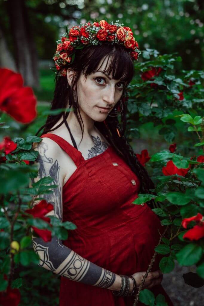 Schwangere in rotem Kleid mit Dreadlocks vor Rosenbusch