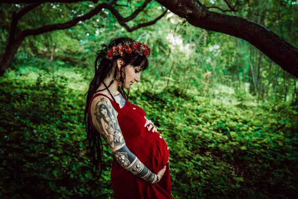 Schwangere in rotem Kleid steht im Wald