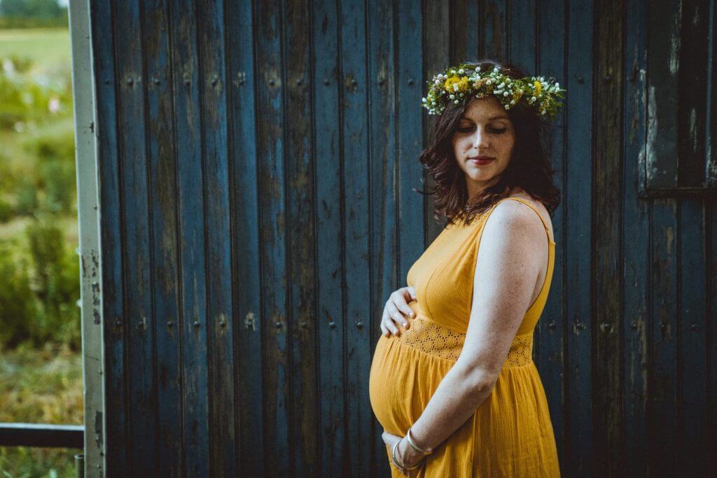 Schwangere steht vor blauer Holzwand und blickt auf ihre Schulter