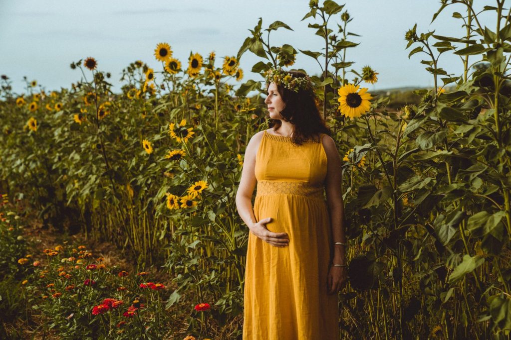 Schwangere steht vor Sonnenblumenfeld