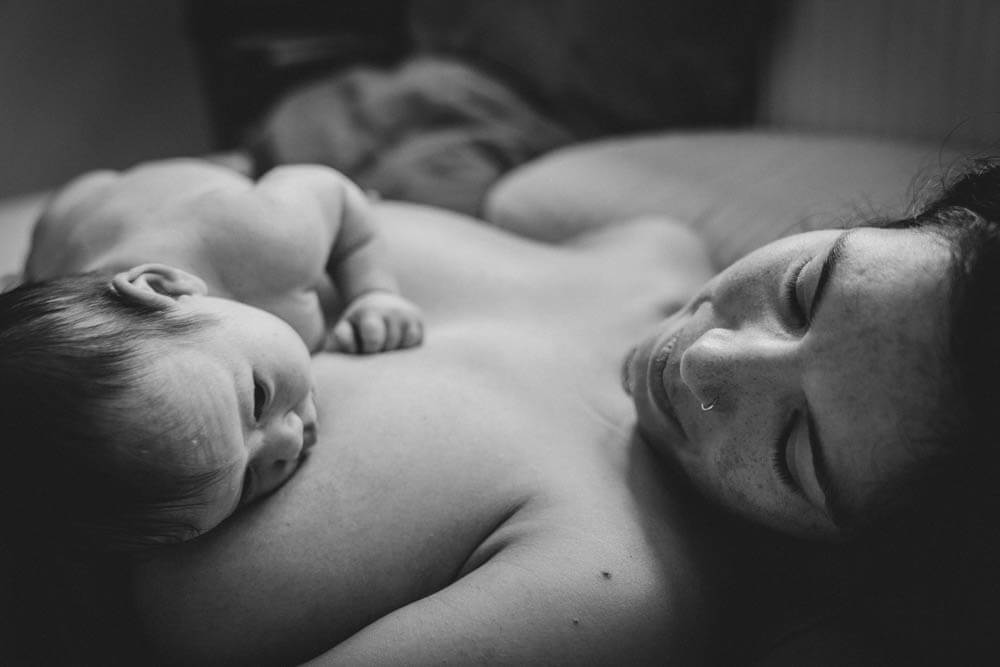 Baby liegt auf Mamas Brust und schaut Mutter an
