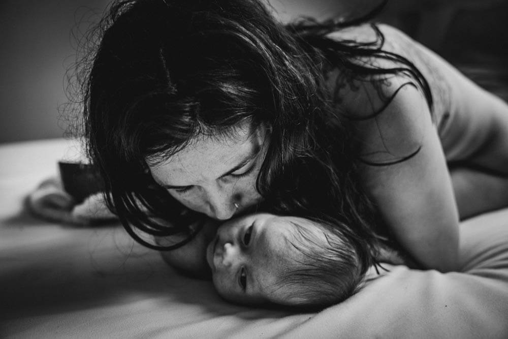 Mama küsst Baby auf dem Bett