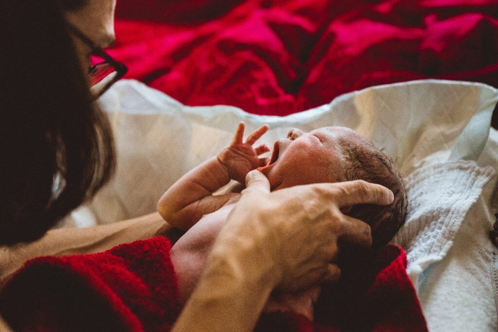 Neugeborenes wird nach Hausgeburt von Hebamme untersucht