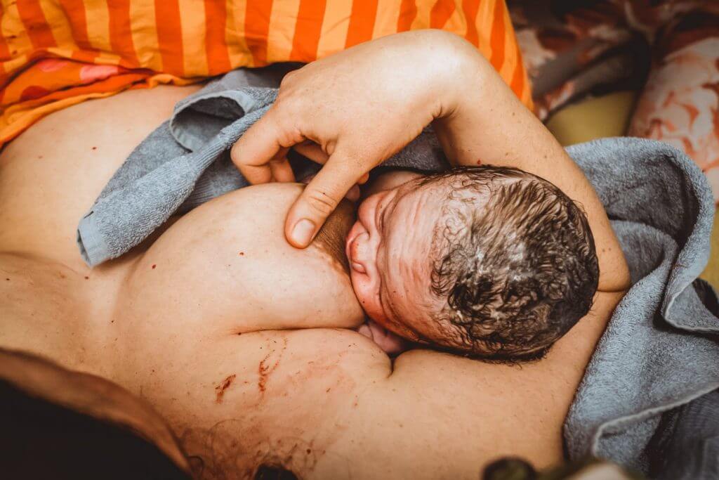 Neugeborenes stillt nach Geburt in orangener Bettdecke