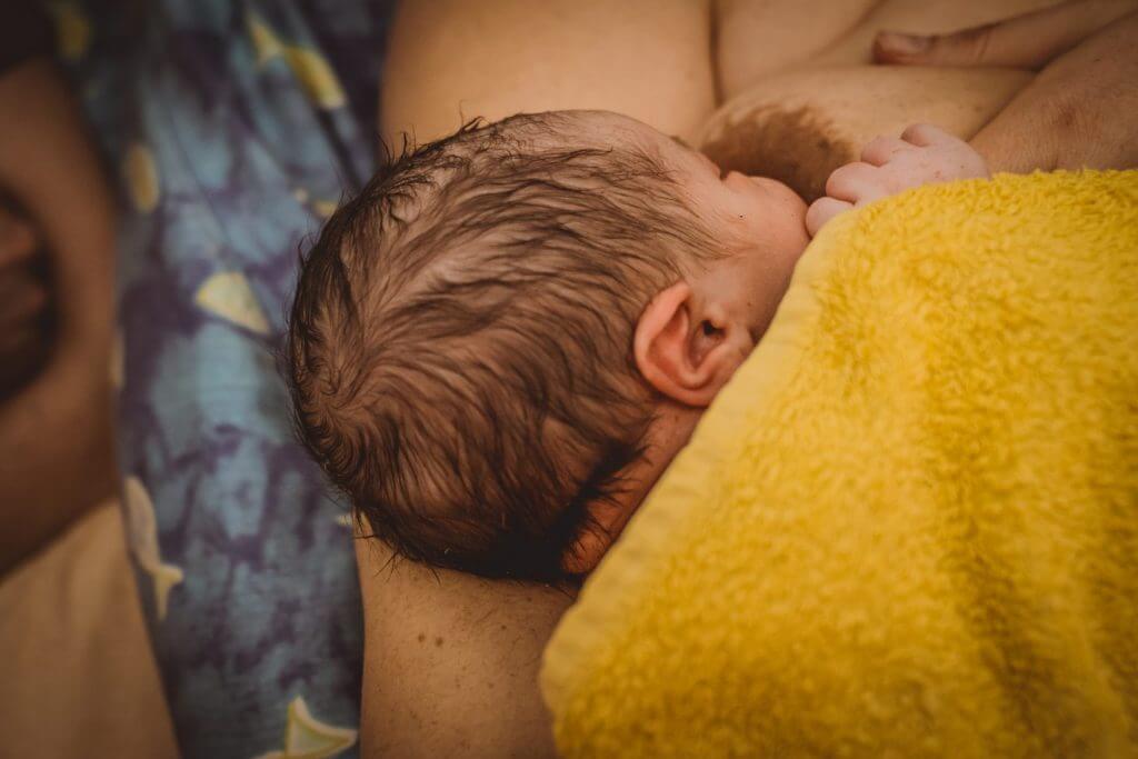 Nahaufnahme Neugeborenenkopf in gelbem Handtuch beim Stillen