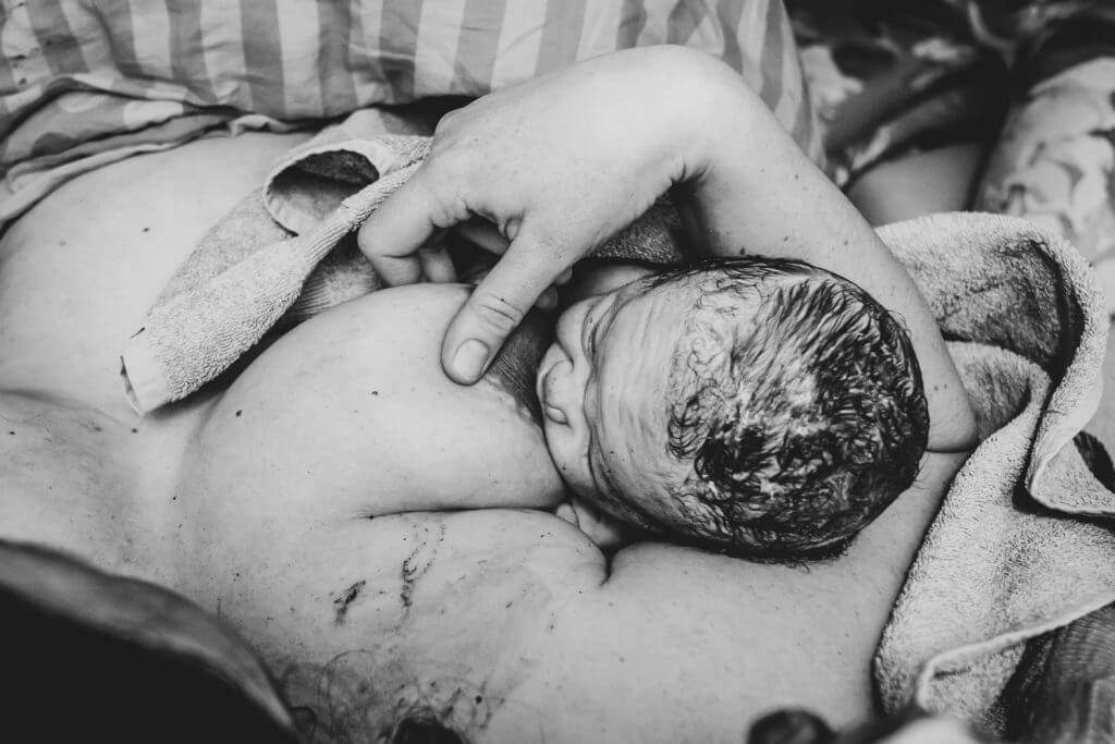 Neugeborenes stillt nach Geburt in Mamas Armen