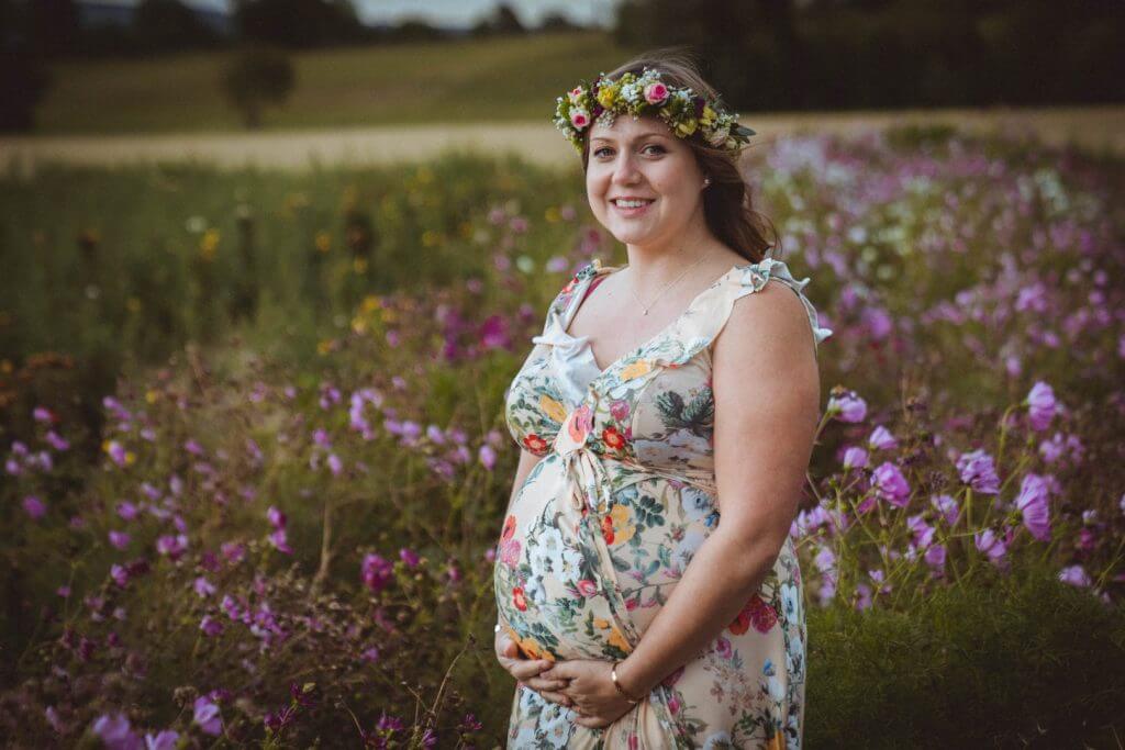 Schwangere hält Bauch in lila Blumenfeld
