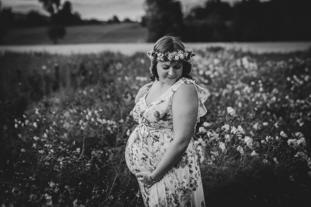 Schwangere steht in Blumenfeld und streichelt Babybauch