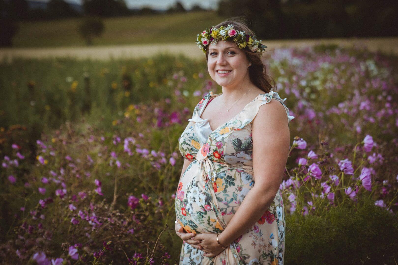 Schwangere hält Babybauch in Blumenfeld