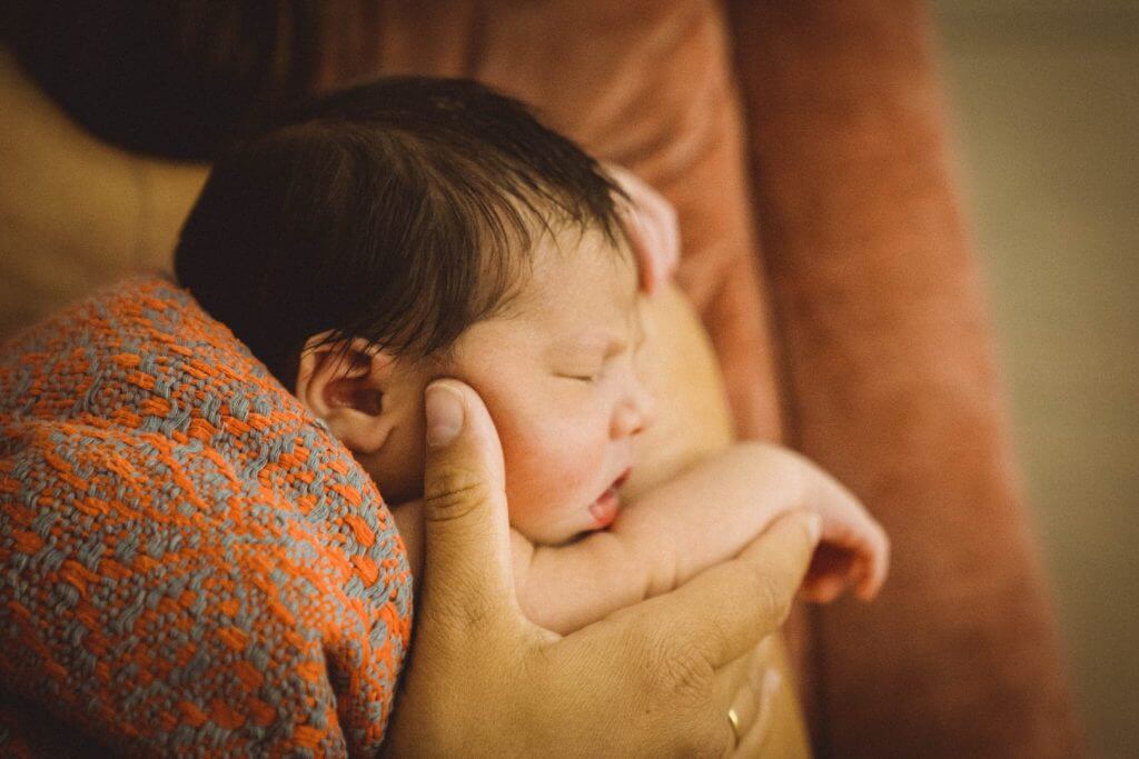 Mutter hält Neugeborenes in rosa Decke an ihrer Schulter