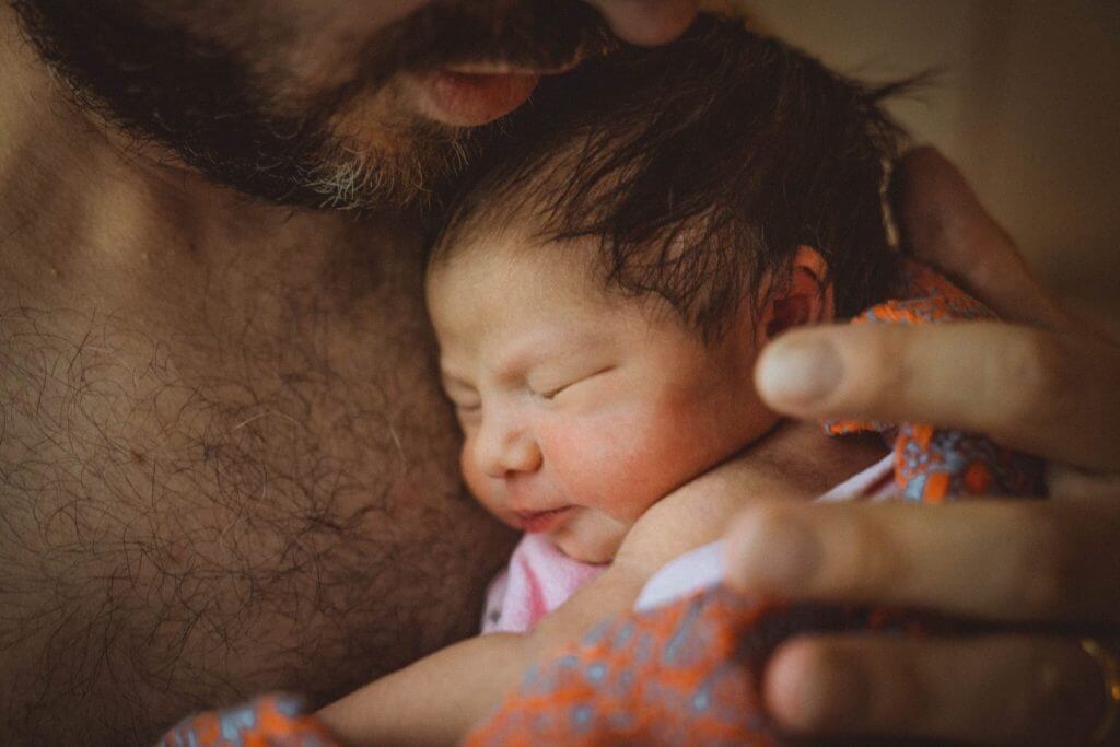 Neugeborenes in rosa Decke lehnt an Papas nackter Brust