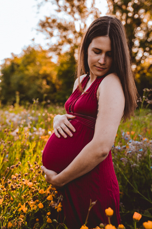 Schwangere steht in Blumenwiese und hält Bauch