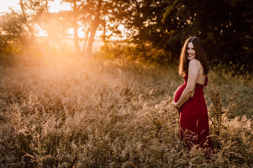 Schwangere lacht und steht in Morgensonne