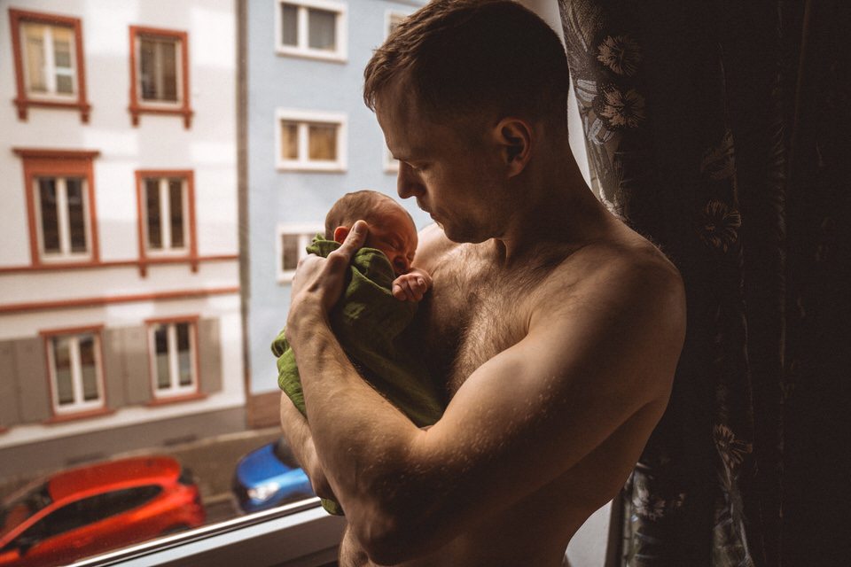 Oberkörperfreier Vater hält Baby am Fenster