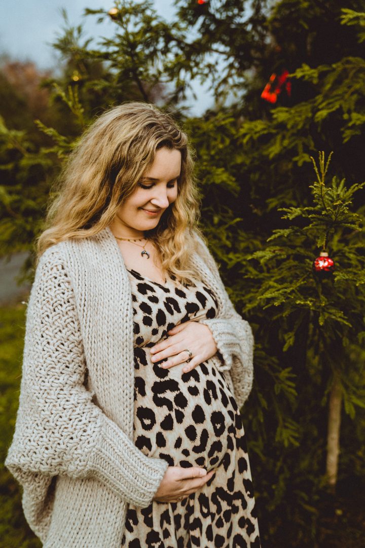 Schwangere blickt auf Babybauch vor Weihnachtsbaum