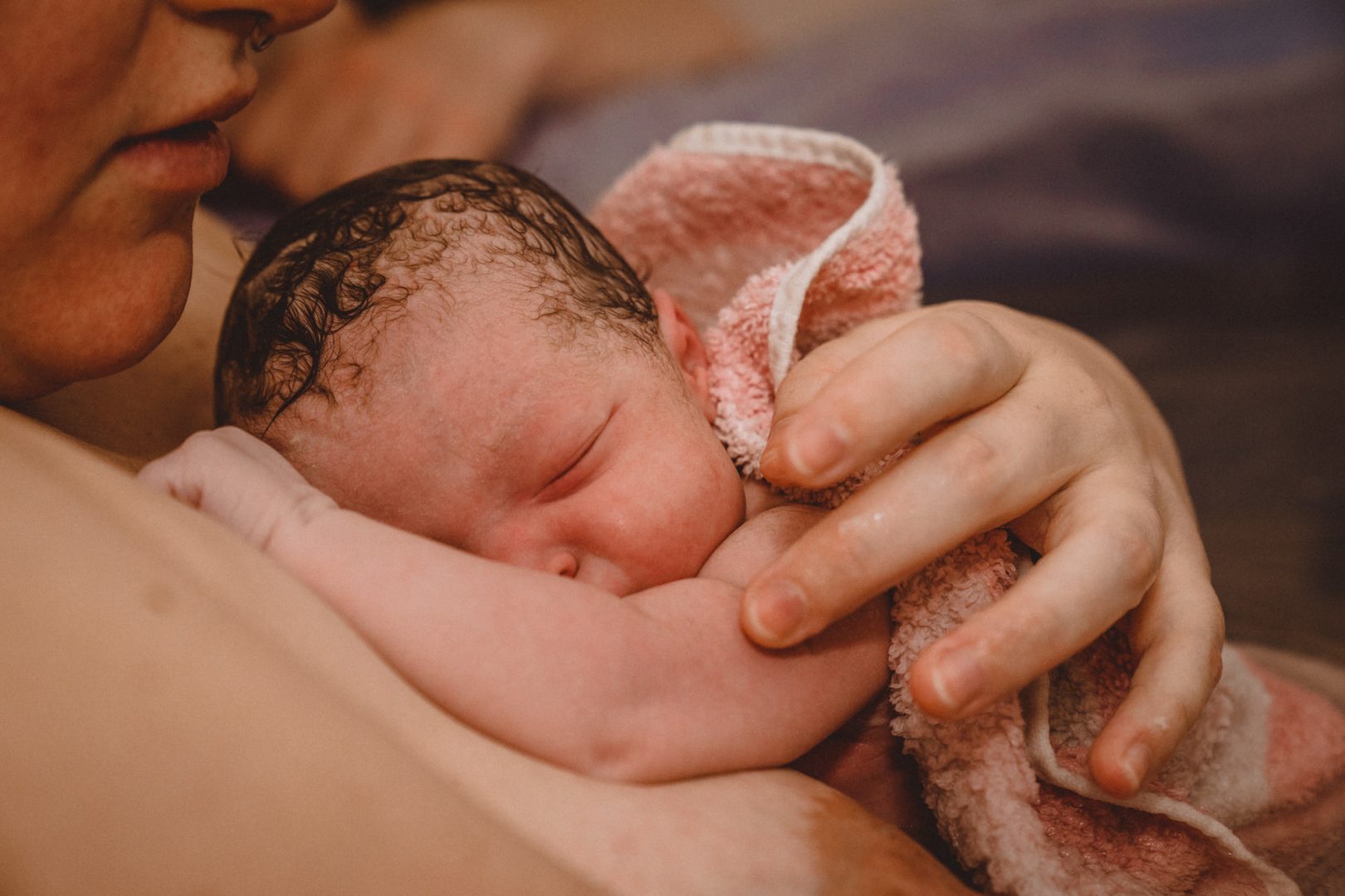 Neugeborenes liegt in rosa Hand auf Brust der Mutter