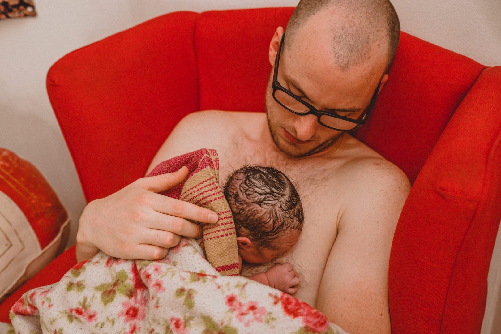 Papa kuschelt mit Neugeborenem in rotem Sessel