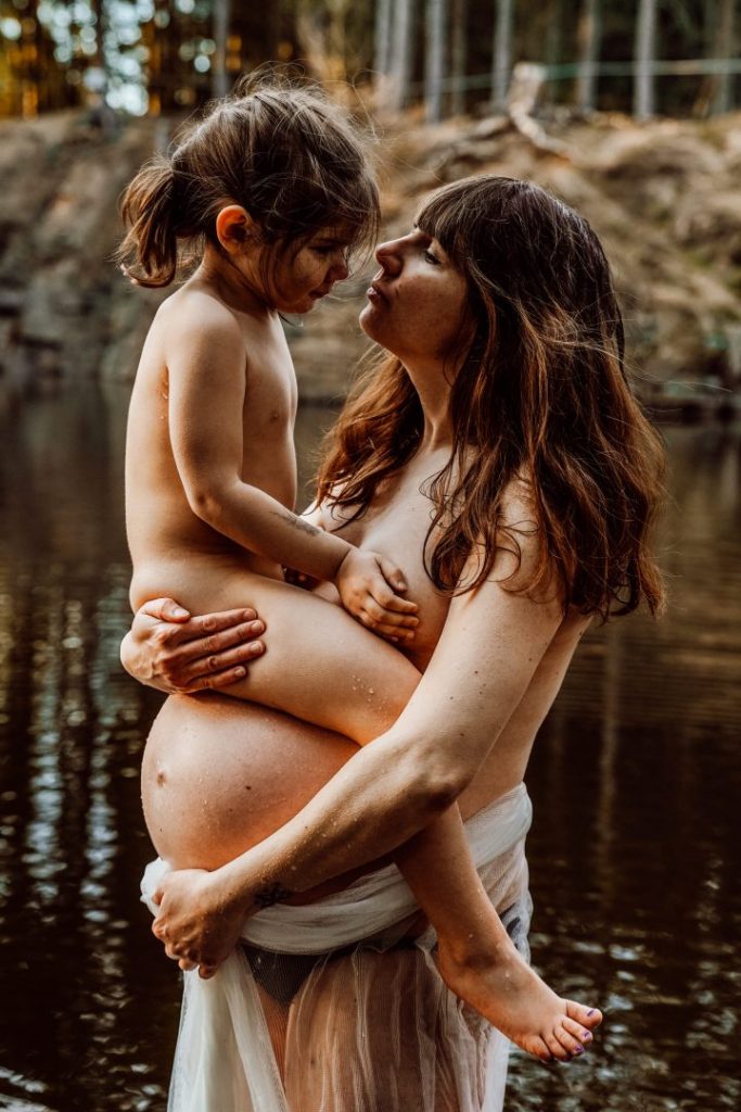 Kind sitzt auf Babybauch im Wasser