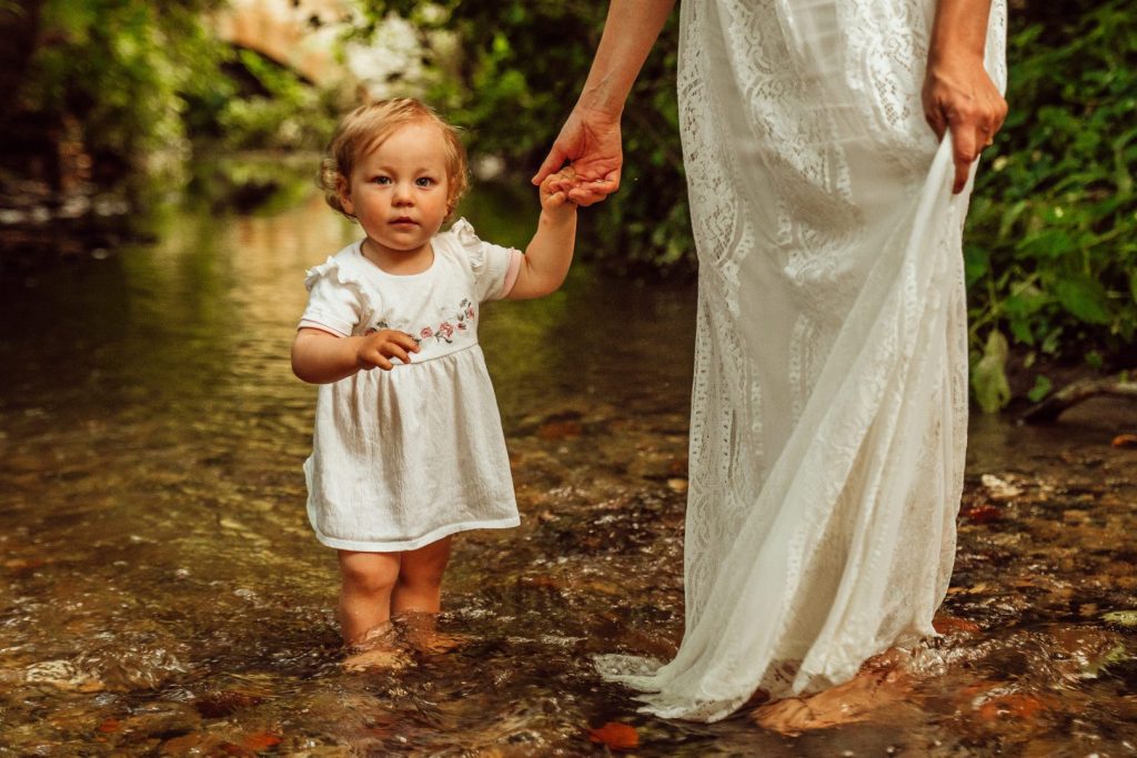 Kleinkind steht in Bach und hält Hand seiner Mutter