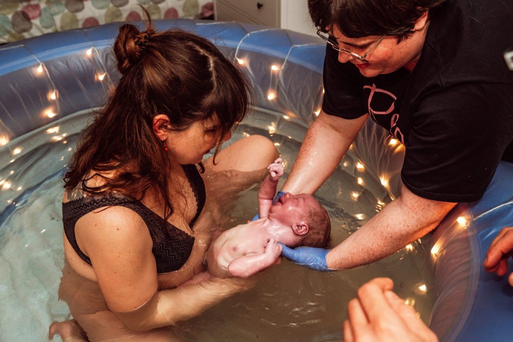 Mama hebt Baby mit Hebamme aus dem Wasser