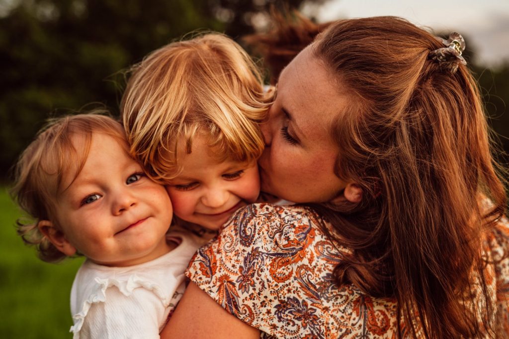 Mama küsst ihre Kinder auf ihrem Arm